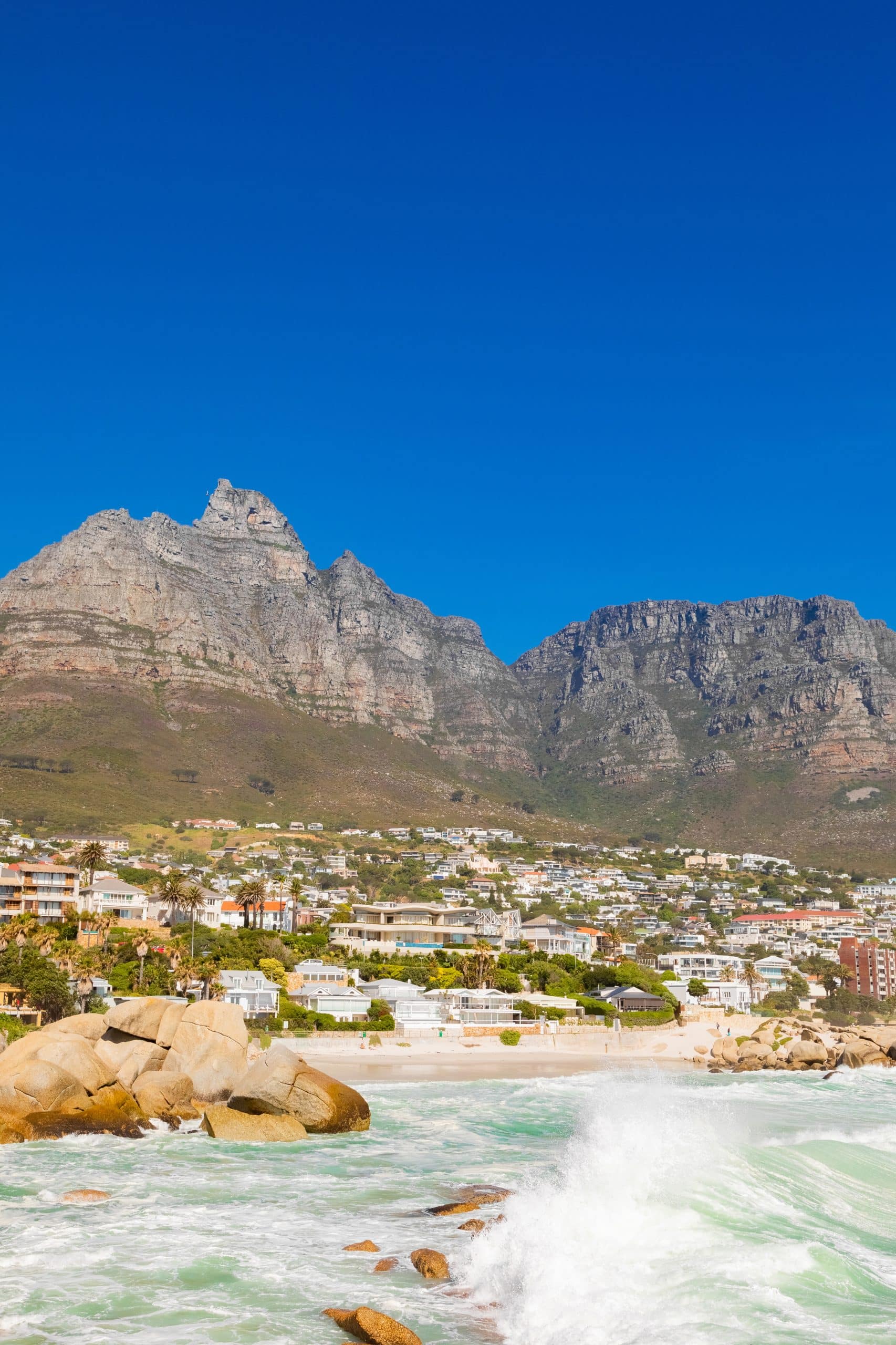 Privacy en Herstel: Waarom Kiezen voor een Buitenlandse Afkickkliniek? Coastal view of mountains and beach with waves crashing on rocks under a clear blue sky.