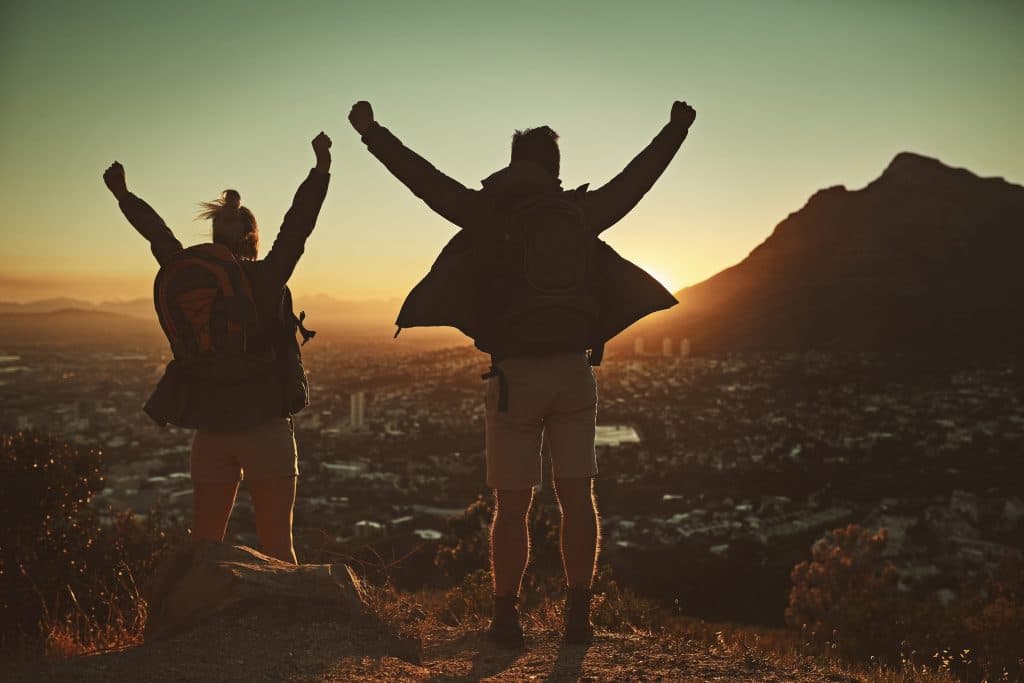 Verslavingszorg in Zuid-Afrika: Waar Moet Je Op Letten? Two hikers celebrating at sunrise on a mountain overlooking a cityscape in South Africa.